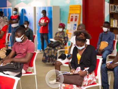 People wearing masks seated indoors, maintaining social distancing.